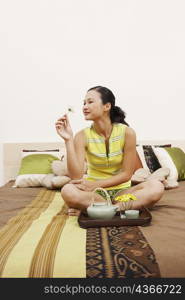 Young woman sitting on the bed and looking at a flower