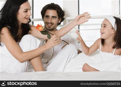 Young woman sitting on the bed holding a flower with a young man and her daughter
