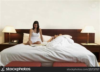 Young woman sitting on the bed with a mid adult man sleeping beside her