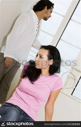 Young woman sitting on the bed with a young man standing behind her