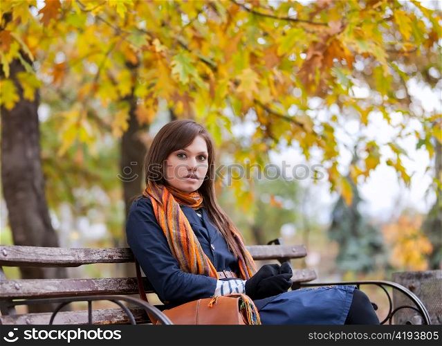 Young woman sitting on the bench in autumn park