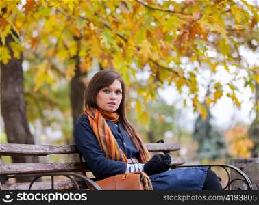 Young woman sitting on the bench in autumn park