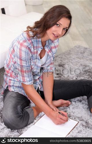 young woman sitting on the carpet and writing