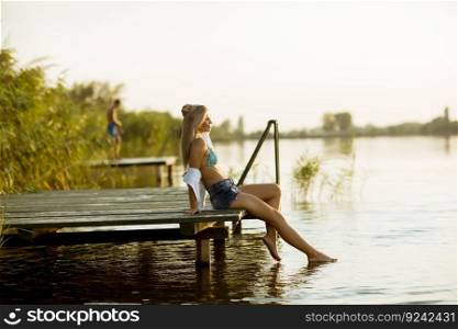Young woman sitting on the pier on the lake at sunset