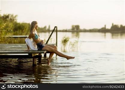Young woman sitting on the pier on the lake at sunset