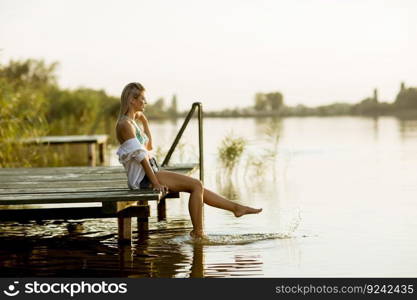 Young woman sitting on the pier on the lake at sunset