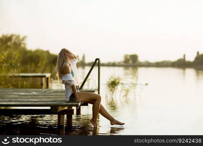 Young woman sitting on the pier on the lake at sunset