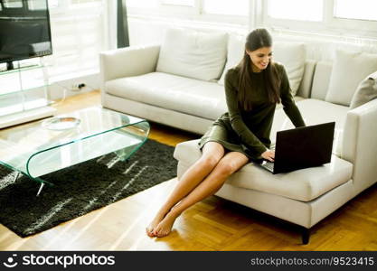 Young woman sitting on the sofa in the room and using laptop