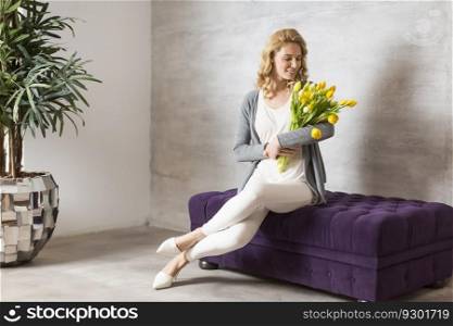 Young woman sitting on the sofa with a bouquet of yellow tulips