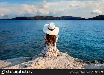 Young woman sitting on the top of rock and looking at the seashore.