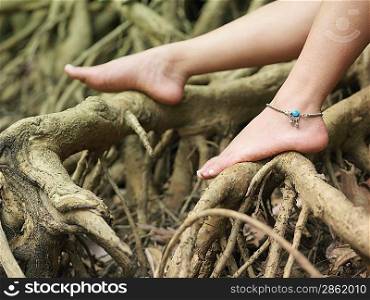 Young woman sitting on tree roots close-up on foot