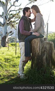 Young woman sitting on tree stump, boyfriend standing in front
