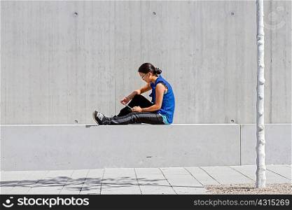 Young woman sitting on wall reading digital tablet