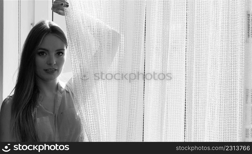 Young woman sitting on windowsill looking through window enjoying her free time, relaxing.. Woman looking through window, relaxing