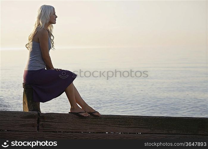 Young woman sitting on wooden bale on beach, side view