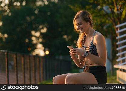 Young woman sitting outdoors, wearing earphones, looking at smartphone