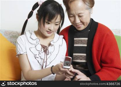 Young woman sitting together with her grandmother holding a mobile phone