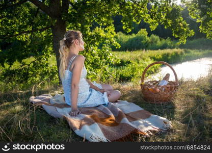 Young woman sitting under big tree at field and looking at lake