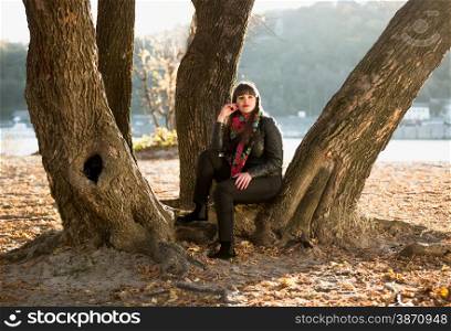 Young woman sitting under tree at autumn park next to river