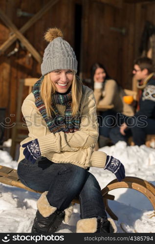 Young woman sitting winter snow sledge cottage spending holiday friends