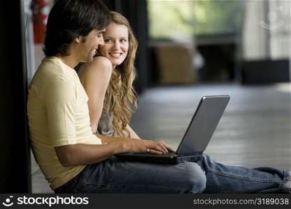 Young woman sitting with a young man working on a laptop