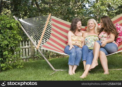 Young woman sitting with two mature women in a hammock and smiling