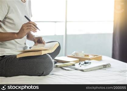 Young woman sitting working and writing in the notebook on bed leisure concept taking notes, Comfortable female workplace. Memories, planning , education