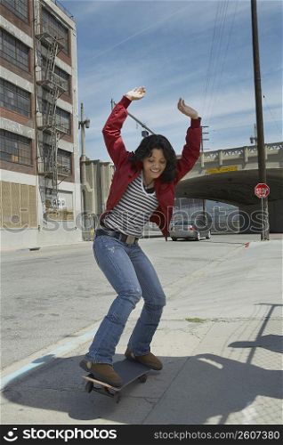Young woman skateboarding at a roadside with her arms raised