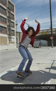 Young woman skateboarding at a roadside with her arms raised
