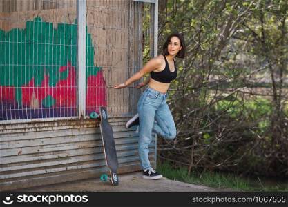 Young woman skater grabs ancient metal fence in a ancient industrial street, freedom concept