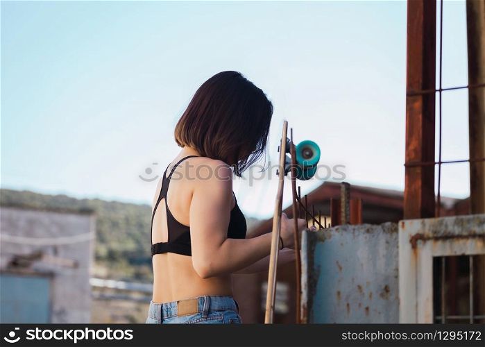 Young woman skater trying to climb over the fence look inside in a ancient industrial street
