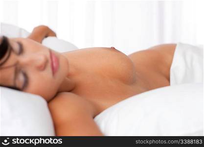 Young woman sleeping in white bed, focus on nipple, shallow DOF