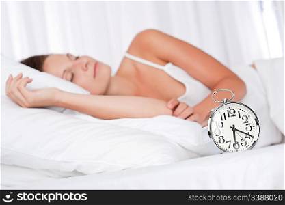 Young woman sleeping in white bed with alarm clock
