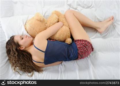 Young woman sleeping on a bed in an embrace with teddybear