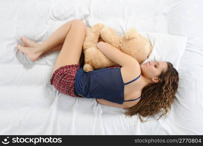 Young woman sleeping on a bed in an embrace with teddybear