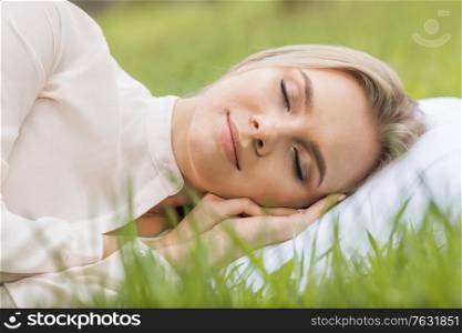 Young woman sleeping on soft pillow in fresh spring grass. Woman sleeping on pillow in grass
