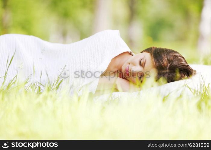 Young woman sleeping on white pillow in fresh spring grass
