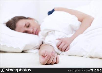 Young woman sleeping soundly in bed, focus on her outstretched hand on the mattress