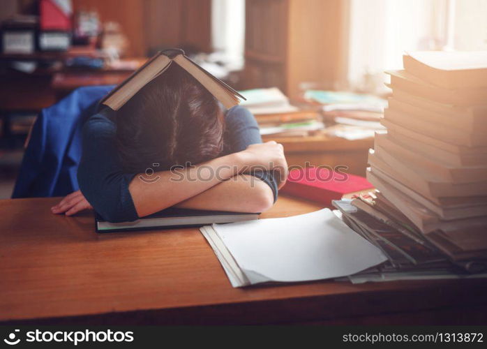 Young woman sleeping with a book on her head in the library. Lifestyle before examen.