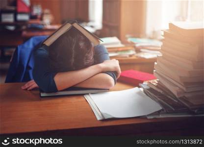 Young woman sleeping with a book on her head in the library. Lifestyle before examen.