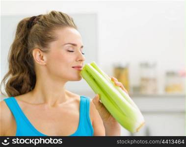 Young woman smelling celery in kitchen