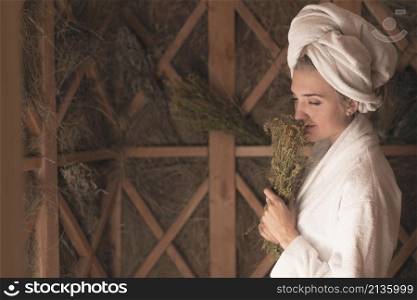 young woman smelling herb flowers standing sauna