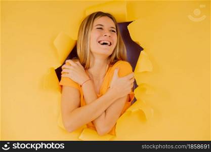 Young woman smiling and embracing to herself while stands through a hole on the paper wall.
