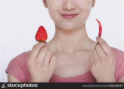Young woman smiling and holding opposites, a strawberry and a chili pepper, in each hand