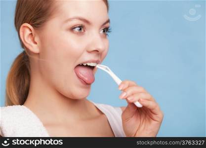 Young woman smiling girl with cleaner cleaning her tongue on blue. Daily dental care and oral hygiene. Studio shot.