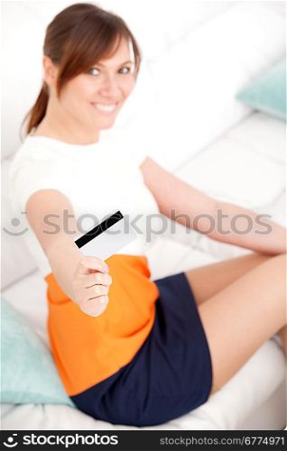young woman smiling into camera with card in hand sitting on sofa in living room