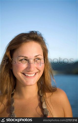 Young woman smiling, looking off camera, water in the background