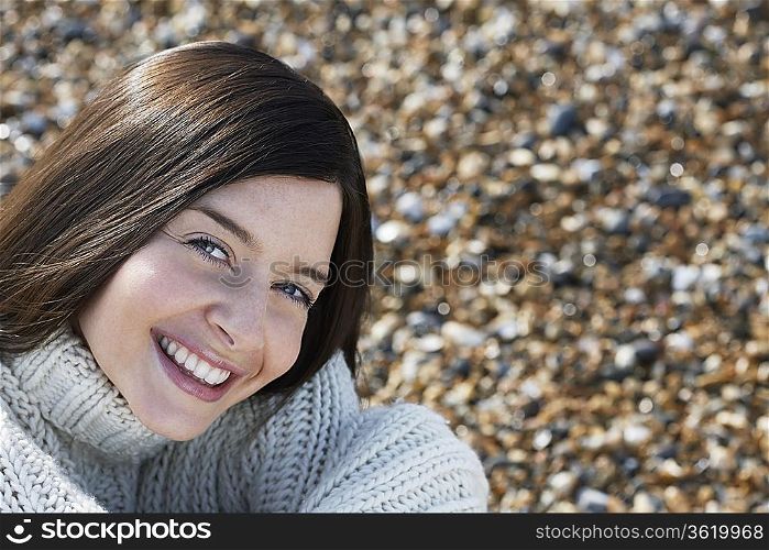 Young woman smiling, sitting on beach, close-up
