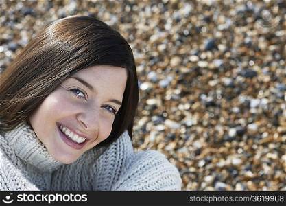 Young woman smiling, sitting on beach, close-up