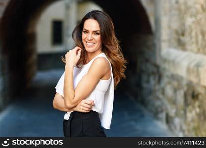 Young woman smiling to camera outdoors. Female in casual clothes with care hairstyle in Granada, Andalusia, Spain.. Happy young woman smiling to camera outdoors.